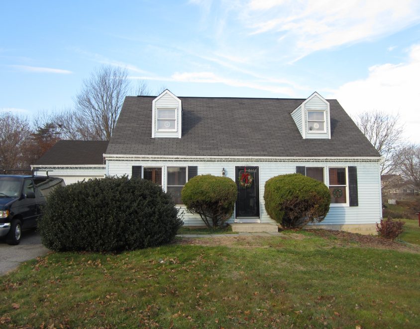 light blue home with holiday decoration on front door and shrubberies in front yard